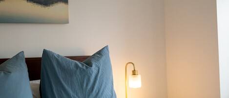 Une chambre d’hôtel avec un lit, deux oreillers, une table de chevet avec une lampe et un tableau au mur.
