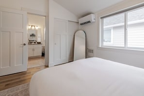 A bedroom with a bed, a white door, a window, and an air conditioning unit.