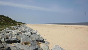 Une plage dont le premier plan est constitué de rochers et qui s’étend sur une étendue de sable jusqu’à la mer, sous un ciel dégagé.