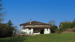 A two-story house with a tiled roof, a stone chimney, and a small porch with outdoor seating. - Maison de l'olivier - Rural Comfort & Relaxation (Champniers-et-Reilhac)