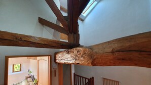 A room with exposed wooden beams, a bed with a green and white checkered bedspread, a nightstand with a lamp, and a view of another room through an open door. - Maison de l'olivier - Rural Comfort & Relaxation (Champniers-et-Reilhac)