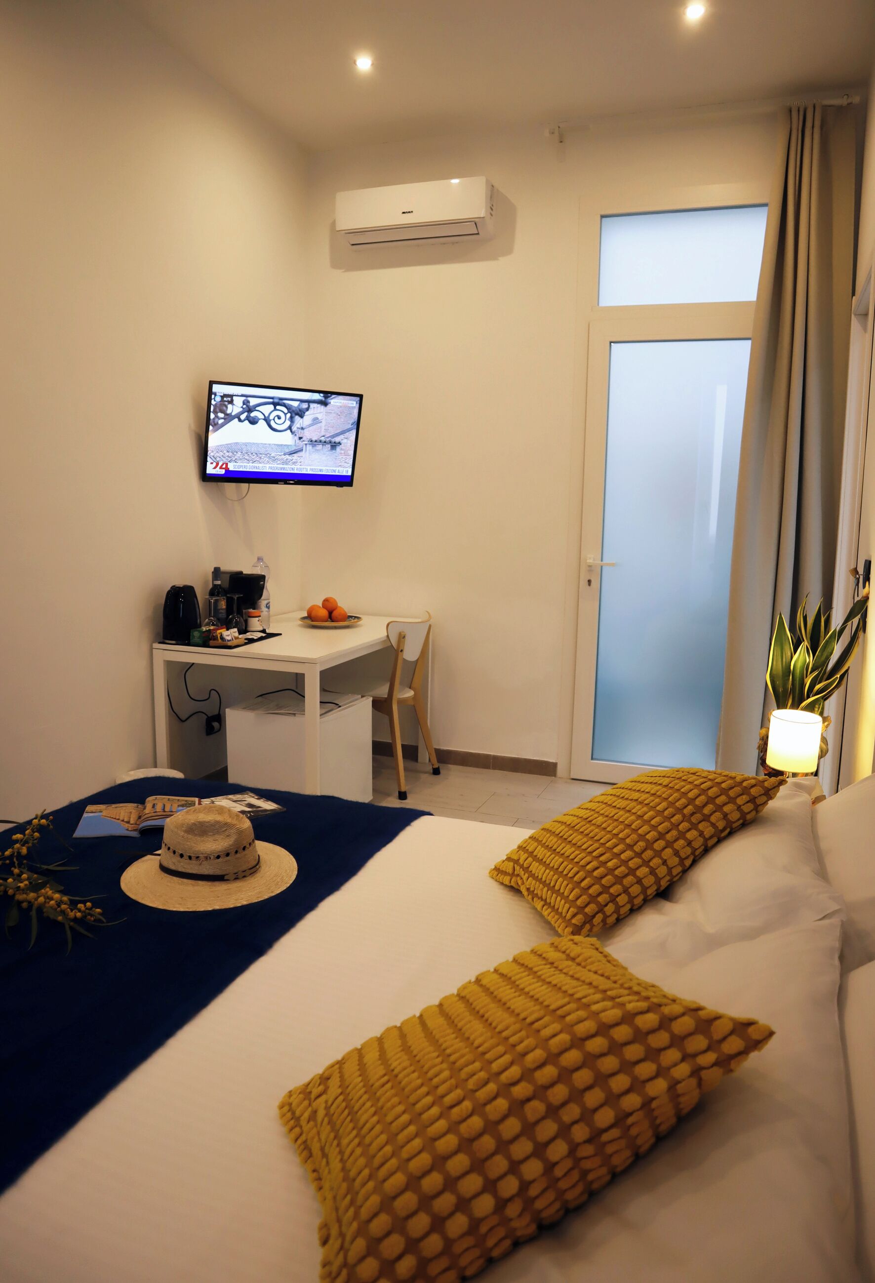 A hotel room with a bed, a desk, a television, a plant, and a sliding door.