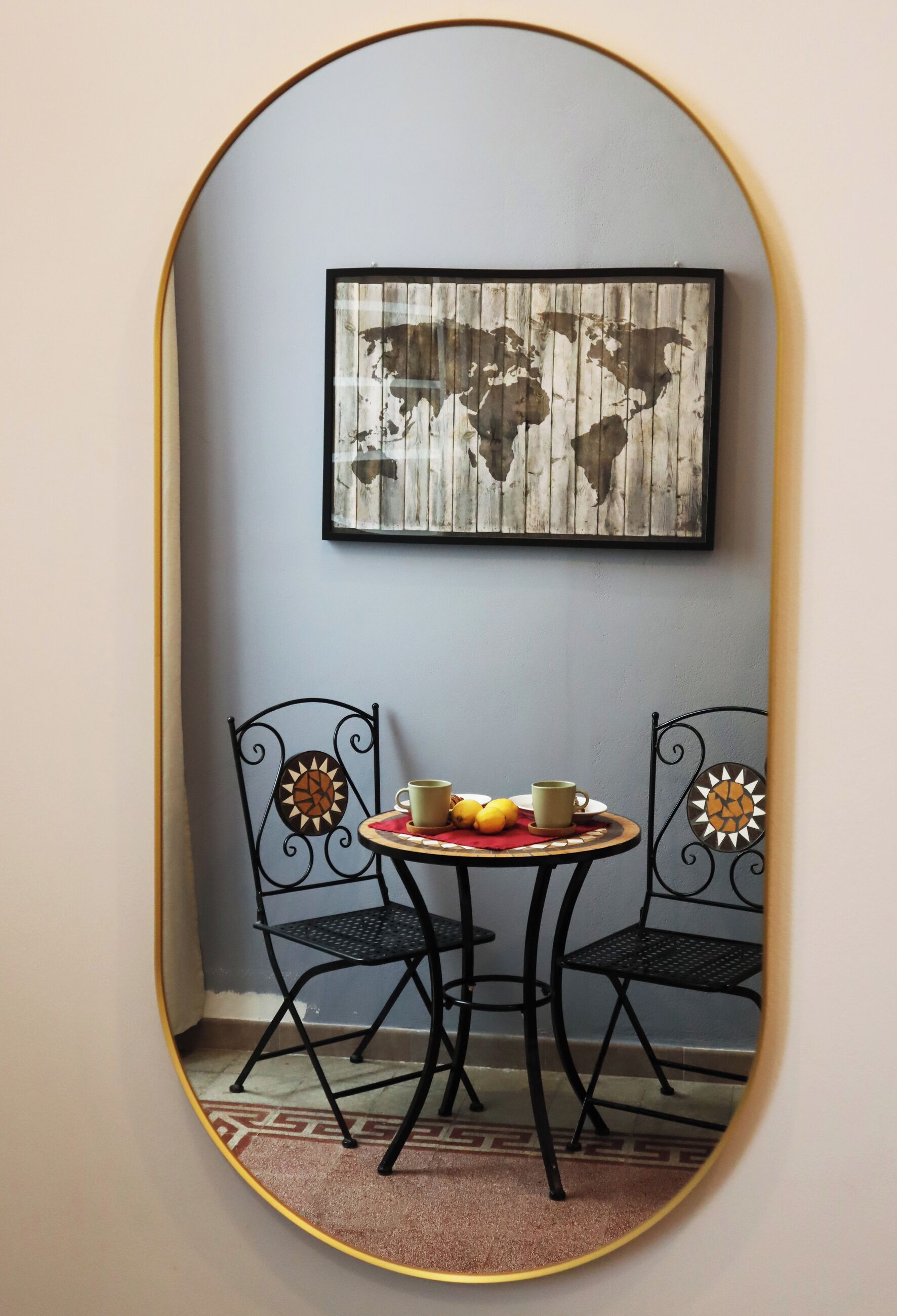 Een kamer met een ronde tafel, twee stoelen, een wereldkaart in een lijst en een spiegel die de kamer weerspiegelt.
