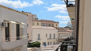 A balcony with potted plants, a white chair, and a table with a plate and cup. - Fortuna Guest House (Syracuse)