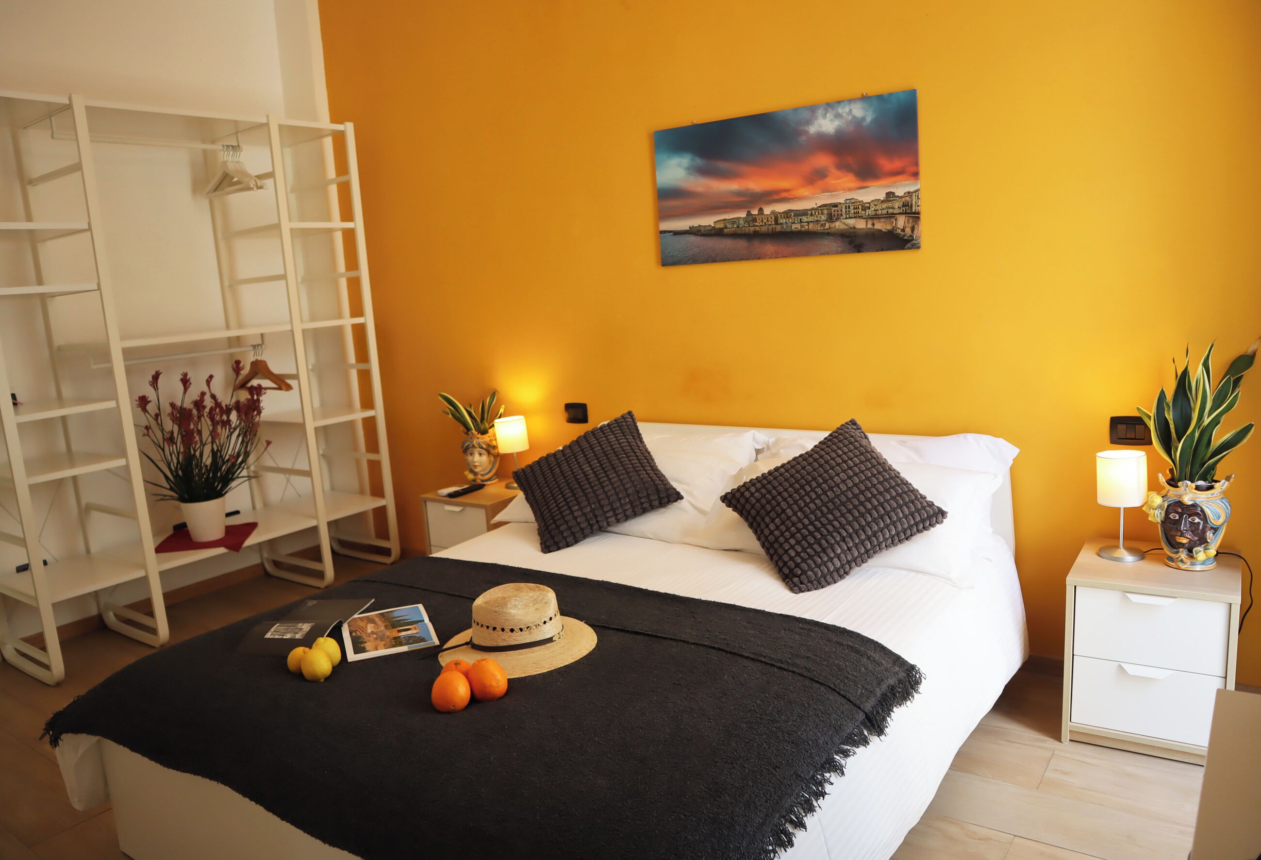 A bedroom with a bed, a nightstand, a lamp, a potted plant, and a painting on the wall.