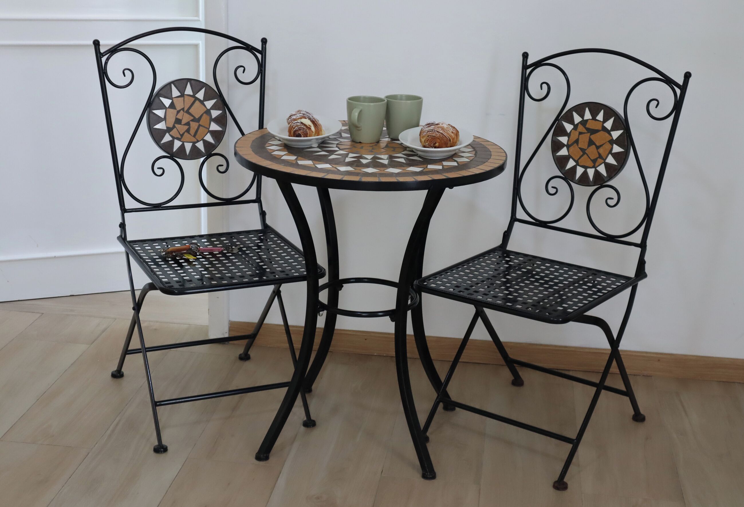 Une table ronde en métal, accompagnée de deux chaises, chacune dotée d’un dossier orné d’un motif géométrique.