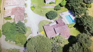 Vue aérienne d’une propriété comprenant une grande maison, plusieurs bâtiments plus petits et une piscine.