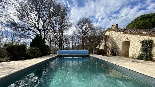 Une piscine rectangulaire à l’eau claire, entour ée de murs en pierre et d’arbres.
