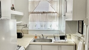 A compact kitchen with white cabinets, a built-in oven, a sink, and a window with decorative curtains.