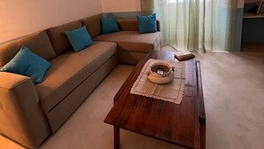 A living room with a beige sectional sofa, two teal pillows, a wooden coffee table with a decorative bowl, and a bookshelf against the wall. - Finished house, 100sqm 10 min from the beaches, 500 m from the historic center of Ugento (Ugento)