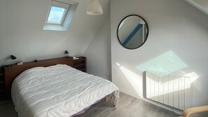 A bedroom with a bed, a small window, a round mirror, and a radiator.