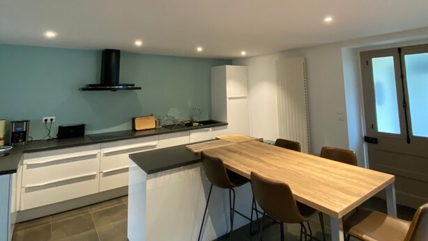 A modern kitchen with a central island, white cabinetry, and a dining area with a wooden table and chairs.