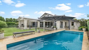 A modern house with a swimming pool, covered patio, and a well-maintained lawn.