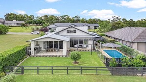A modern two-story house with a covered patio, a swimming pool, and a well-maintained lawn.