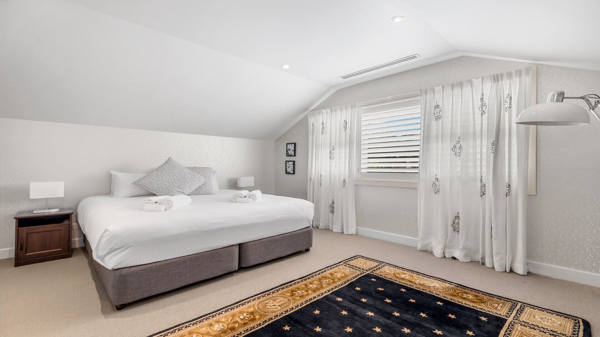 Une chambre à coucher avec un lit, des tables de chevet, une lampe et un tapis.