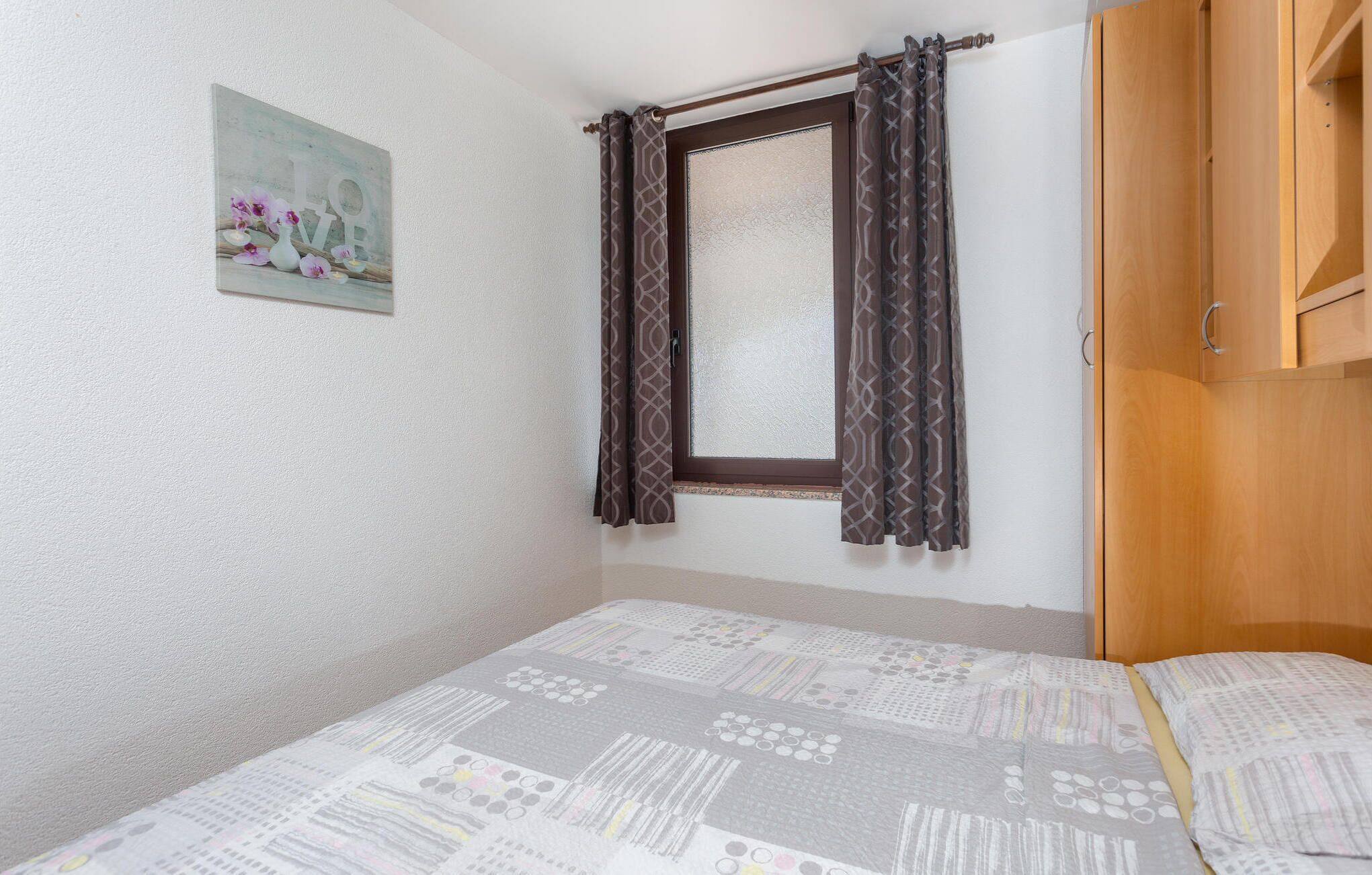 Una camera da letto con un letto, una finestra con tende a motivi, un armadio in legno e un quadro appeso al muro.
