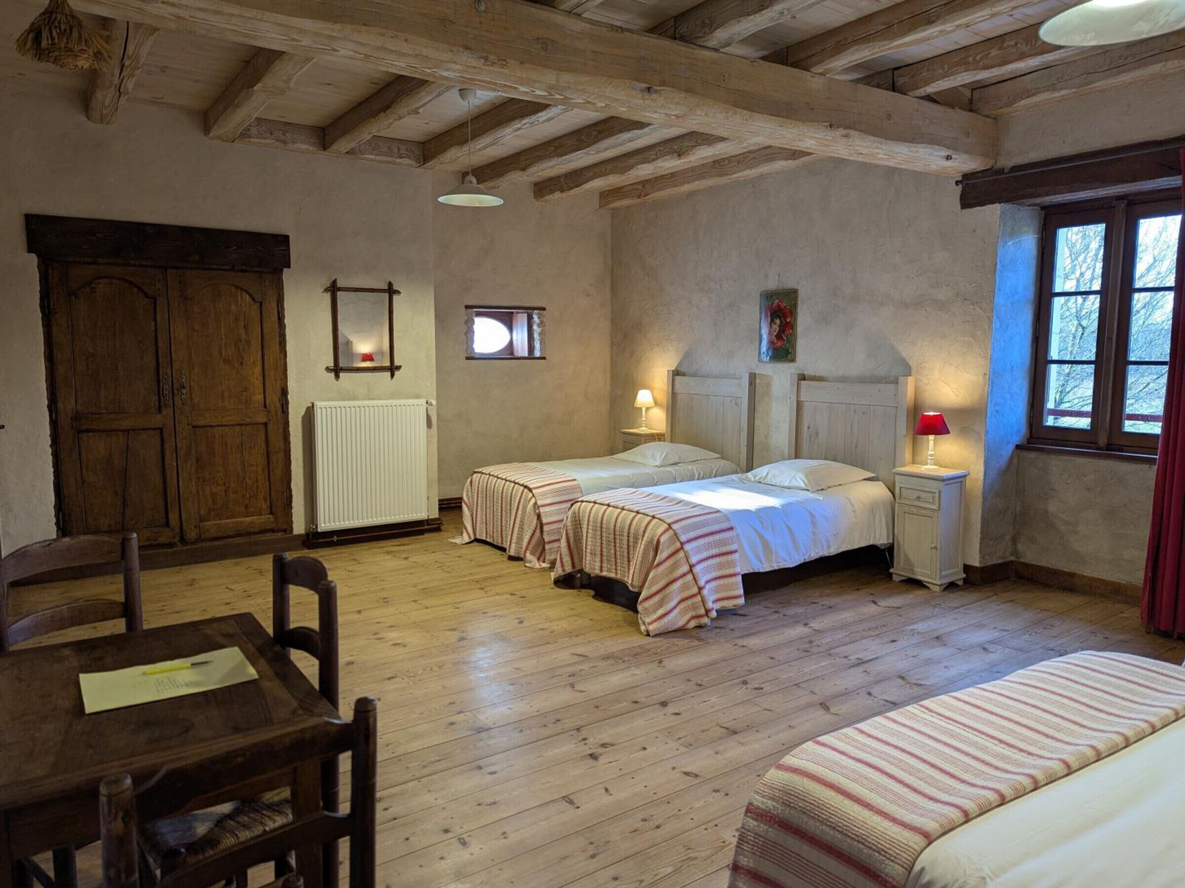 Une chambre rustique avec deux lits, une table en bois et une fenêtre avec des rideaux.