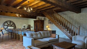 A rustic interior with a wooden staircase, a dining area with a large wheel, a sofa, and a coffee table.