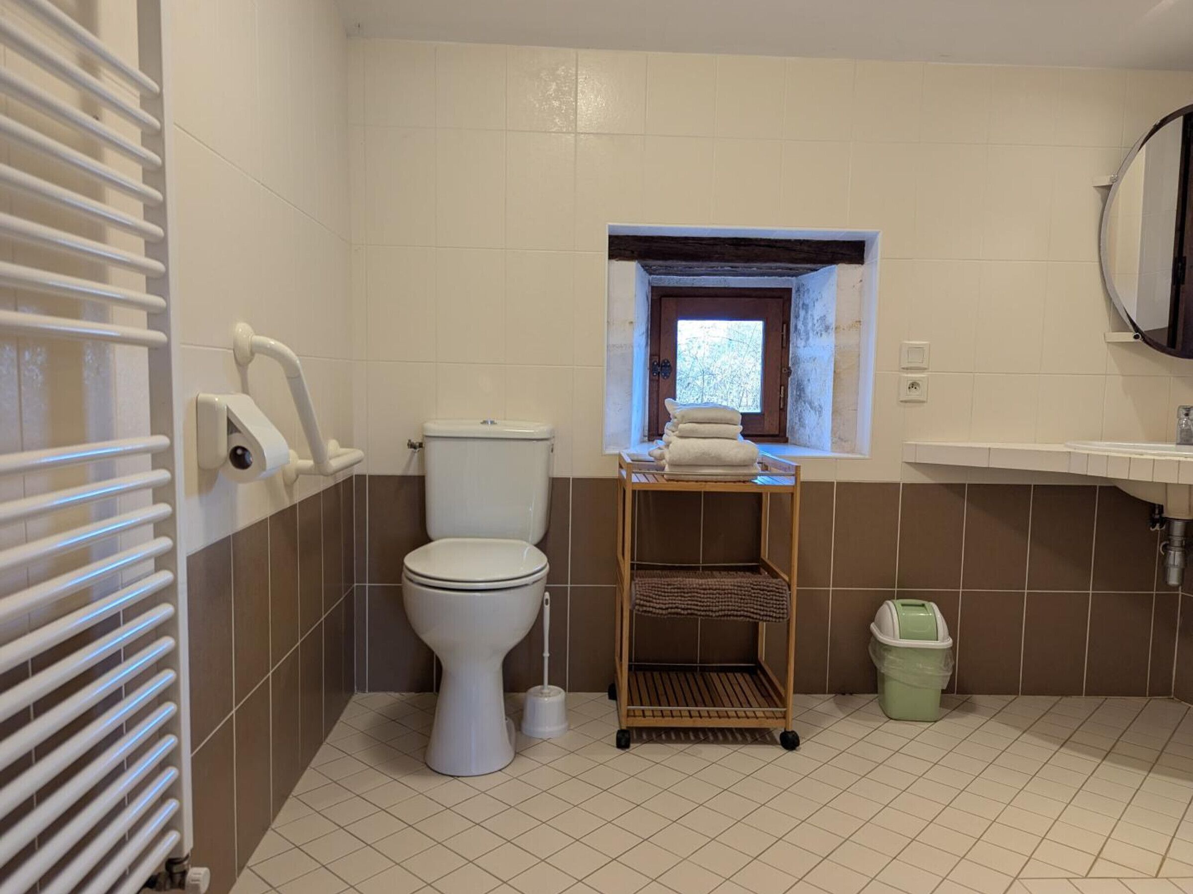 A bathroom with a toilet, a small window, a sink, a radiator, and a trash bin.
