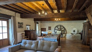 A cozy room with a sofa, a table set for dining, a large wooden wheel, and rustic stone walls.