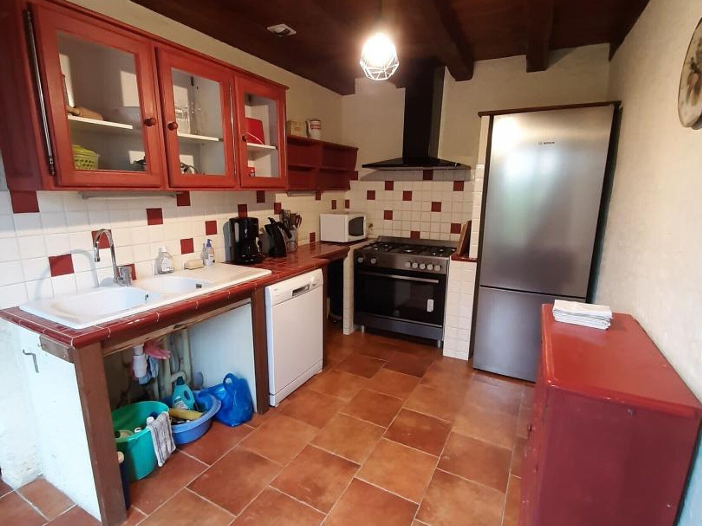 A kitchen with red cabinets, a stainless steel refrigerator, a stove, and a dishwasher.