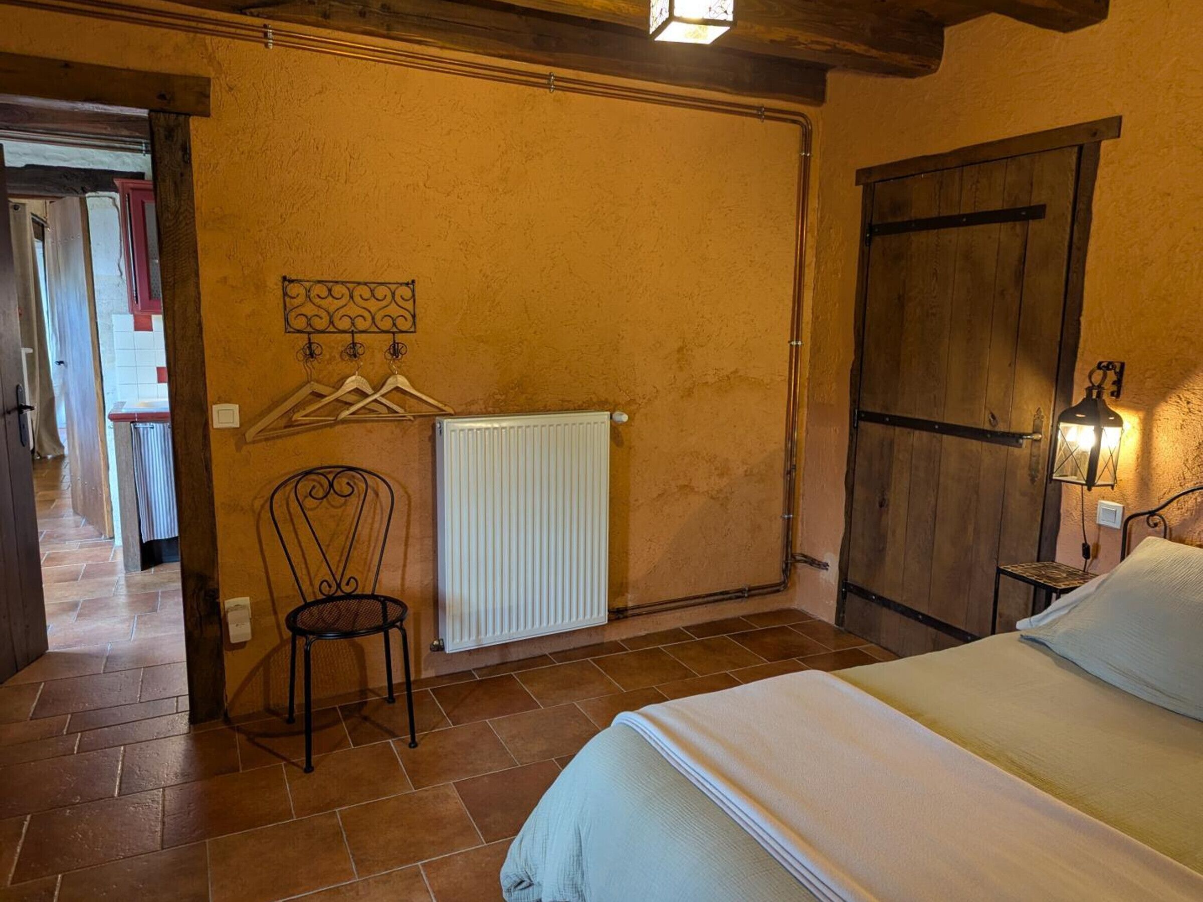 A bedroom with a bed, a radiator, a chair, and a wooden wardrobe.
