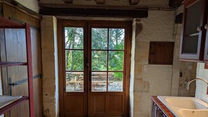 A rustic kitchen with a wooden door, a sink, and a view of an outdoor area with trees.