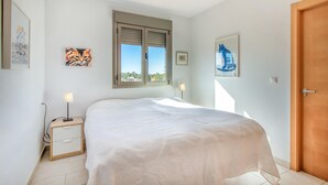 A bedroom with a bed, a nightstand, a lamp, a window with blinds, and artwork on the walls. - Cozy apartment in El Campello with WiFi (El Campello)