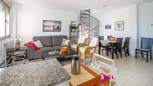 A modern living room with a grey sofa, a coffee table, wicker chairs, a dining table with chairs, a spiral staircase, and a bookshelf. - Cozy apartment in El Campello with WiFi (El Campello)