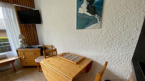 A cozy room with a wooden table, a chair, a small cabinet, a TV mounted on the wall, and a painting above the table. - Studio with Balcony near Bossonnet, La Clusaz - Sleeps 4 with Garage (La Clusaz)