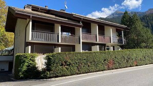 A two-story building with balconies, a hedge in front, and a mountain backdrop. - Studio with Balcony near Bossonnet, La Clusaz - Sleeps 4 with Garage (La Clusaz)