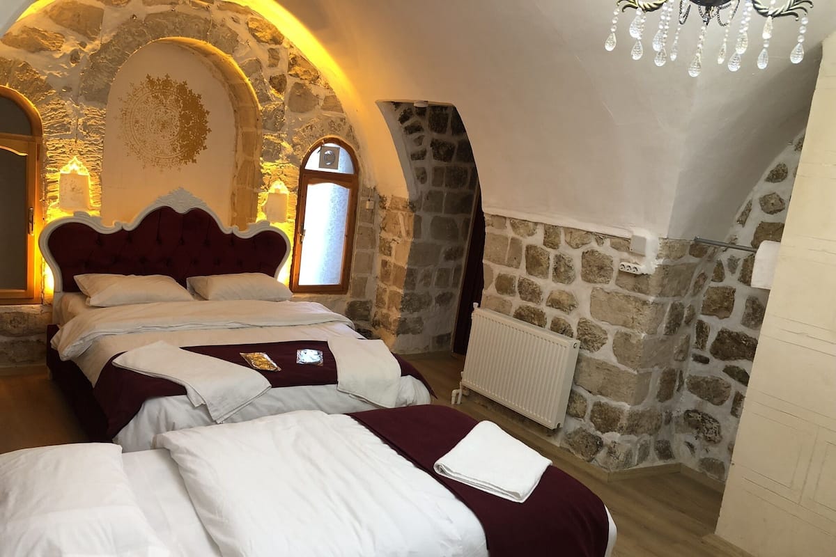 A bedroom with a stone wall, a large bed with white bedding, and a chandelier.