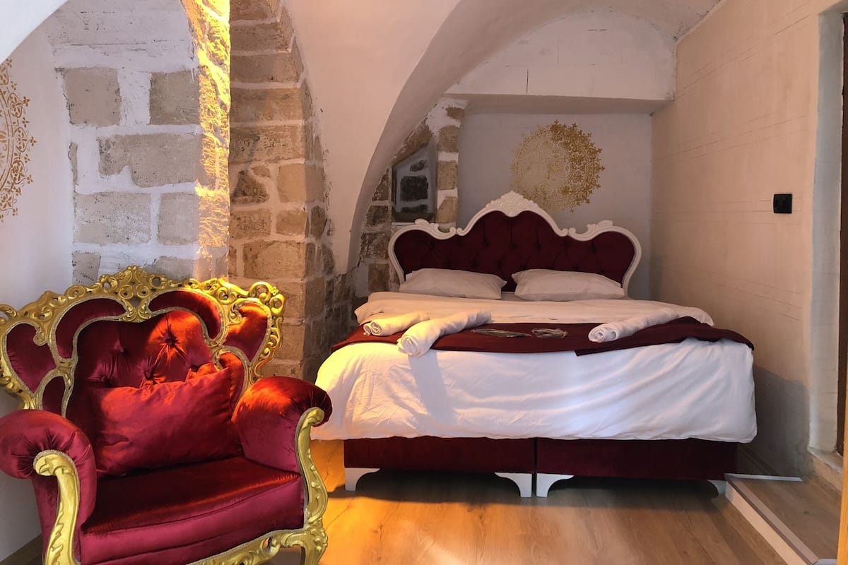 A bedroom with a large bed, a red chair, and an arched stone wall.