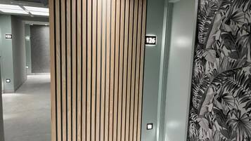 A hallway with a wooden slat partition, a number sign, and a wall with a tropical leaf pattern.