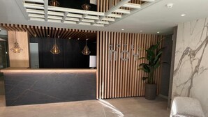 Ein moderner Hotel-Empfangsbereich mit Rezeption, Holzlamellen und einer Zimmerpflanze.