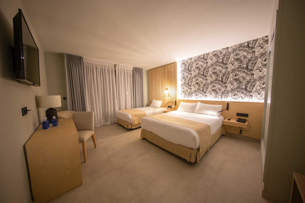 Une chambre d’hôtel avec deux lits, un bureau, une chaise, une télévision et un mur décoré d’un motif.