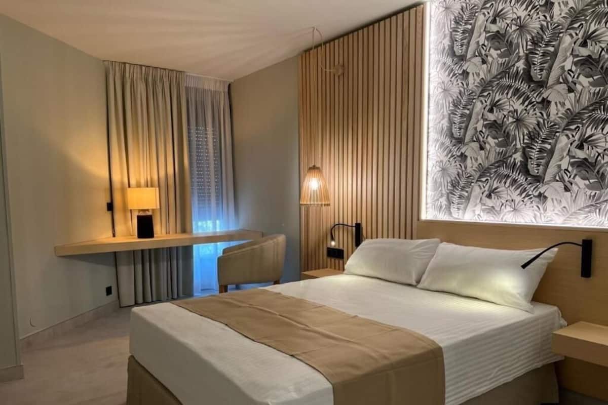 Une chambre d’hôtel moderne avec un grand lit, un bureau et un mur orné d’un motif de feuilles.