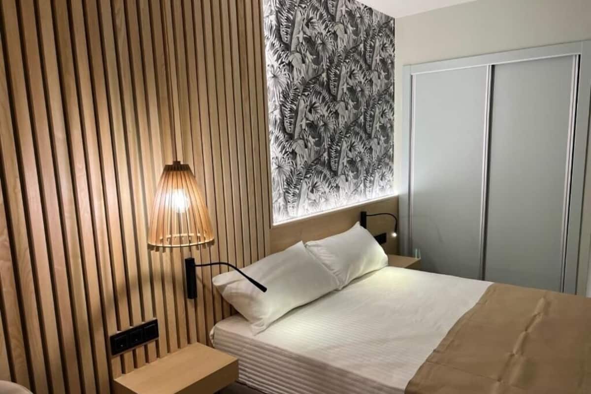 Une chambre à coucher comprenant un lit, une lampe de chevet, un luminaire fixé au mur, un mur décoré d’un motif et une armoire.