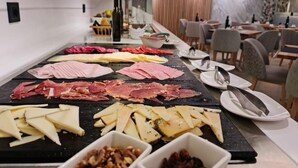 Ein Buffet mit verschiedenen Fleisch- und Käsesorten auf einer schwarzen Servierplatte, umgeben von Esstischen und Stühlen.