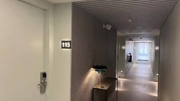 Un couloir moderne avec un panneau indiquant le numéro « 115 » sur le mur, une petite table avec une lampe et un couloir menant à une autre pièce.