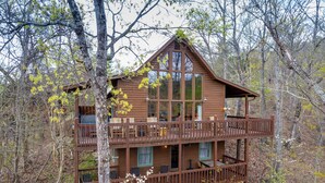 A two-story cabin with a balcony on the upper level, surrounded by trees. - Close to town with private Mountain Setting 3 Bedroom 3 Bathrooom Pet Friendly  Hot tub (Sevierville)