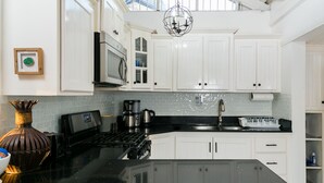 A modern kitchen with white cabinets, a black countertop, a stainless steel stove, and a microwave.