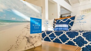Una habitación con una cama que tiene un cubrecolcha azul y blanco estampado, un cabecero de madera y una almohada con un logotipo. En la pared hay un cuadro enmarco con una playa.