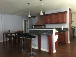 Una cocina con armarios de madera, encimera de granito, ventilador de techo y un taburete de bar.