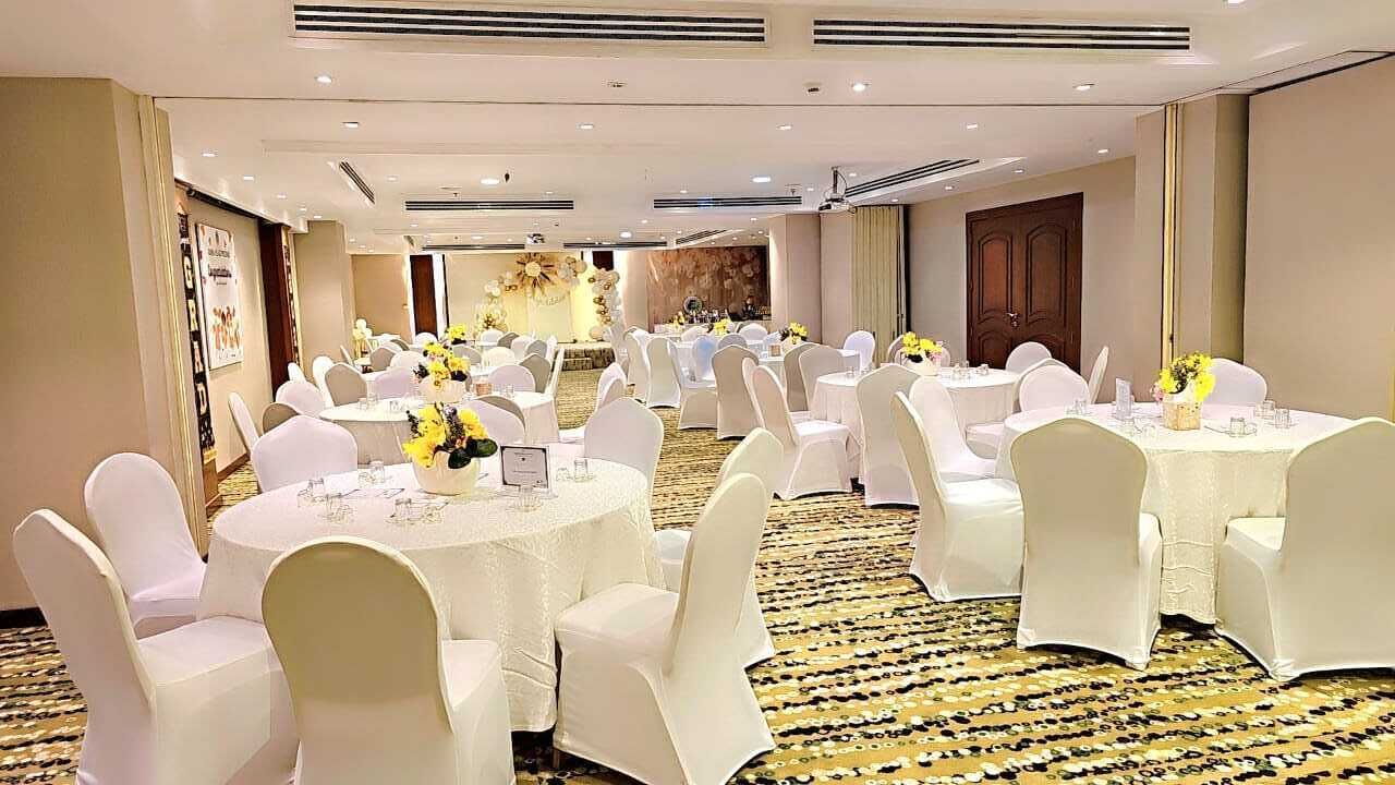 A banquet hall with round tables, white chairs, and floral centerpieces.