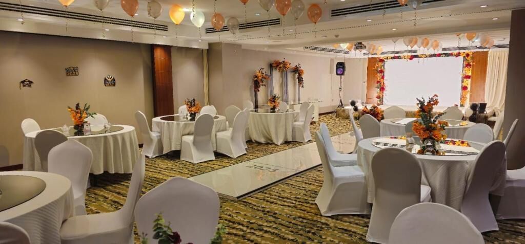 Un salón de banquetes con mesas redondas, sillas blancas y centros de mesa florales.