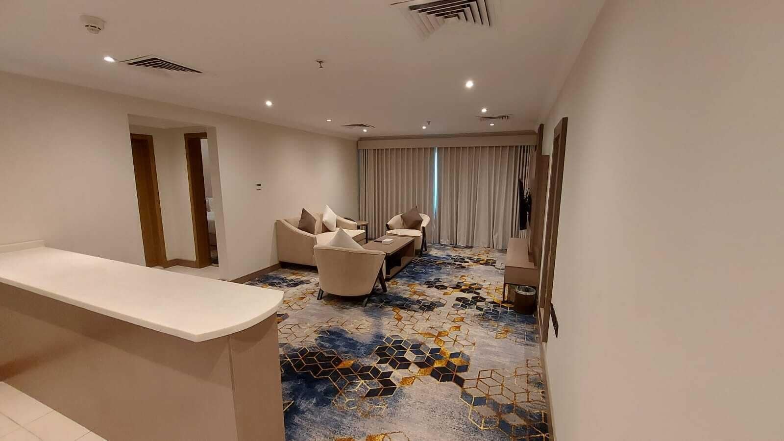 Habitación de hotel con mostrador de recepción, sofá, sillón y alfombra estampada.