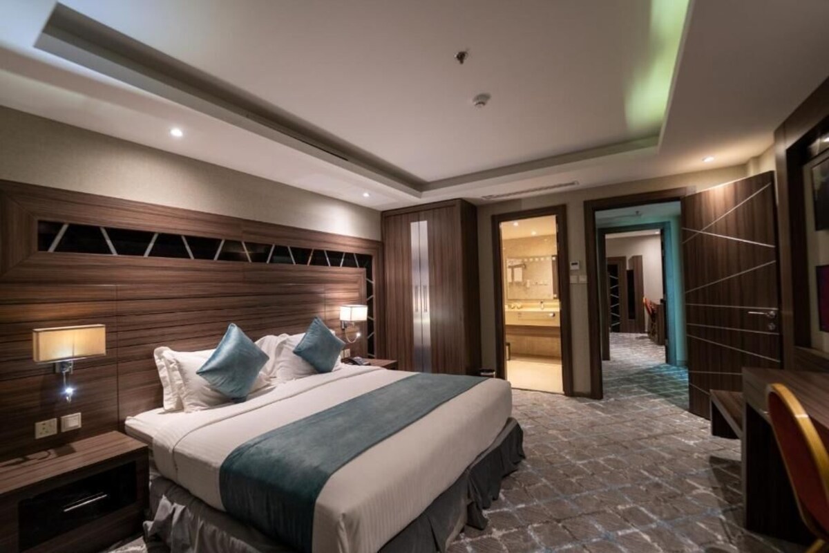 A modern hotel room with a large bed, a nightstand, a desk, and a bathroom visible through an open door.