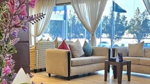 A spacious living room with a sofa, a coffee table, and a view of the outdoors through large windows. - Sumou Hotel Al Khobar (Al Khobar)
