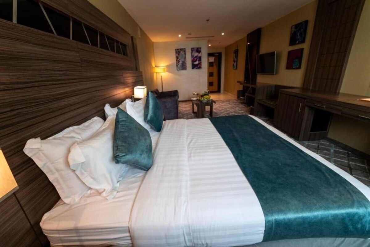 A hotel room with a large bed, a desk, a chair, a lamp, and a television.